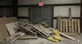 Fire exit door marked "do not block" obstructed by stacked wooden pallets