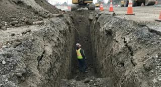 Worker standing inside an open trench with no shoring or trench box installed