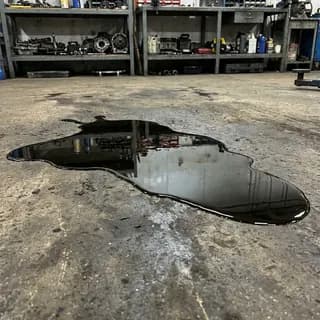 Large dark oil spill spreading across a workshop floor beside metal shelving