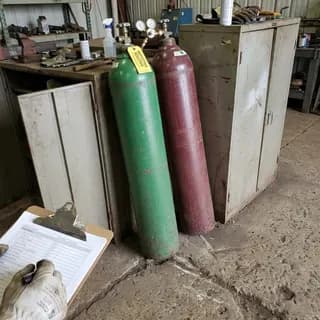 Oxygen and acetylene gas cylinders leaning unsecured against a storage cabinet